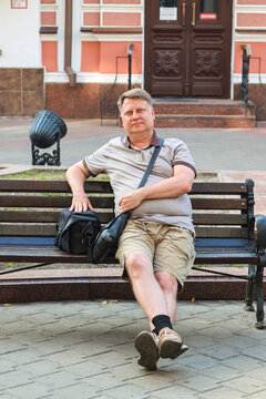 A mature blond man sits happily park bench, enjoying rest and fresh air during the day.