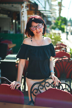 Stylish adult brunette woman off-shoulder blouse on European city street on sunny day, fashion outdoor portrait in urban setting.