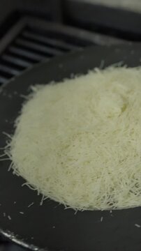 A round mound of fine kunafa pastry heats in a shallow pan above the blue flame of a restaurant gas burner.