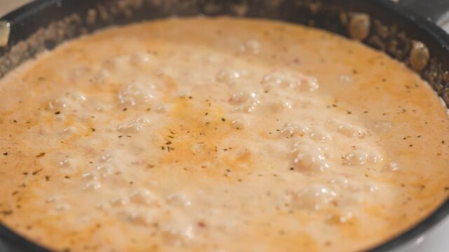 Tomato and garlic sauce with cream and spices bubbling and simmering in pan in home kitchen; process of making tomato pasta; preparation of delicious and healthy Italian meal; food closeup