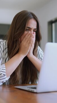 Young frustrated woman feeling stressed and overwhelmed while working on her laptop, receiving bad news, making a mistake online, or experiencing a computer problem at her home office