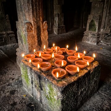 Multiple traditional clay oil lamps burning with bright flames on ancient stone temple platform