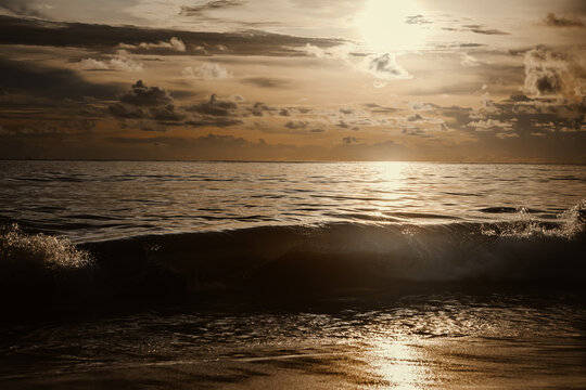 Golden sunset over the sea with sun breaking through clouds and glittering reflection on ocean water
