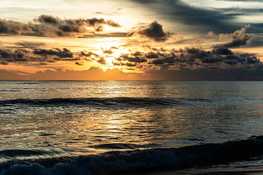 Golden sunset over the sea with sun breaking through clouds and glittering reflection on ocean water