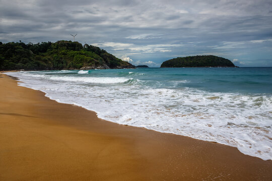 Tropical secluded beach with golden sand, scenic green hill and ocean waves under blue sky