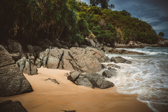 Tropical secluded beach with golden sand, scenic green hill and ocean waves under blue sky