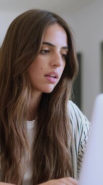 Young businesswoman with a worried expression reacting to bad news on her computer, feeling shocked, stressed, and overwhelmed while working from her home office in a difficult situation