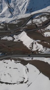 Drone footage of a serpentine asphalt road crossing snowy mountains at Chyyyrchyk Pass. Winter landscape with switchbacks, ridges, and patches of bare ground