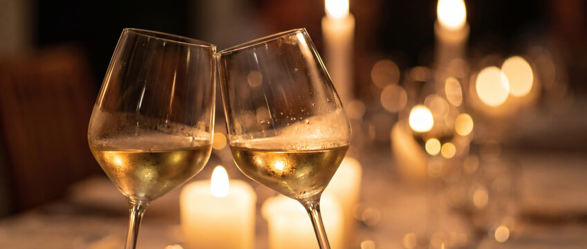 Two wine glasses clink in a warm, candle-lit indoor setting, ideal for intimate celebrations and romantic dinners.