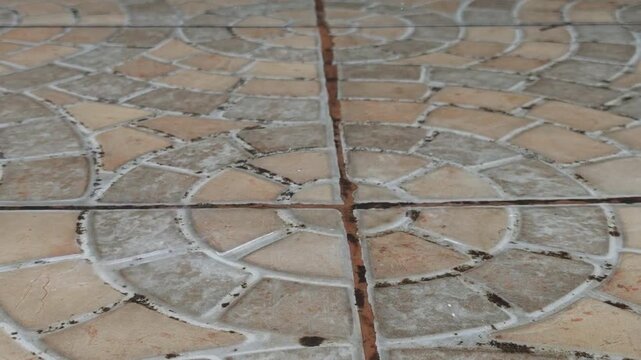 Weathered circular stone paving with irregular tan tile joints forms textured outdoor ground surface, glistening wet after heavy rain in rustic, reflective walkway pattern