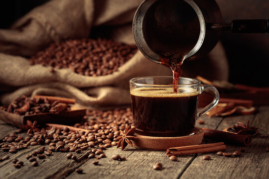 Black coffee is poured from a copper coffee pot into a glass cup.