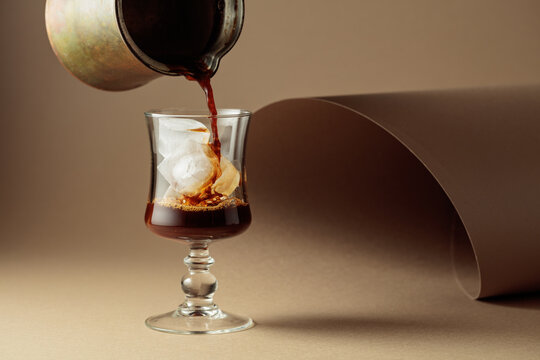 Black coffee is poured into a glass with ice.