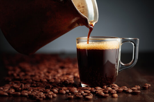 Black coffee is poured into a glass cup.
