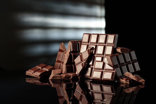 Broken bitter chocolate bars on a black glossy background.