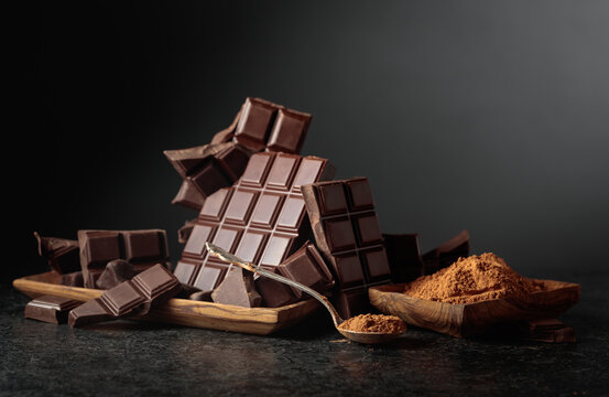 Broken dark chocolate bar and cocoa powder on a black background.