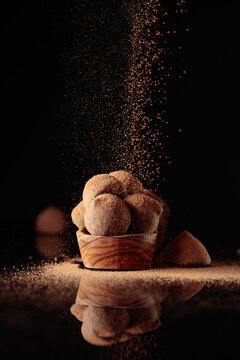Chocolate truffles in small wooden dish sprinkled with cocoa powder. Black reflective background.