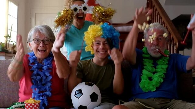Excited multi-generational family fans watching a soccer match on television at home, celebrating a goal with joy and euphoria while throwing popcorn in the air in a moment of happiness