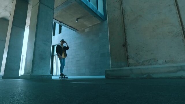 Low-angle perspective of a stylish young man skateboarding on a longboard through a modern concrete underpass, enjoying an active urban lifestyle and his recreational hobby