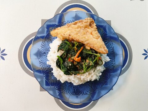 Indonesian traditional rice dish kuluban or pecel with vegetables and crispy fried tempeh served on a blue glass plate."