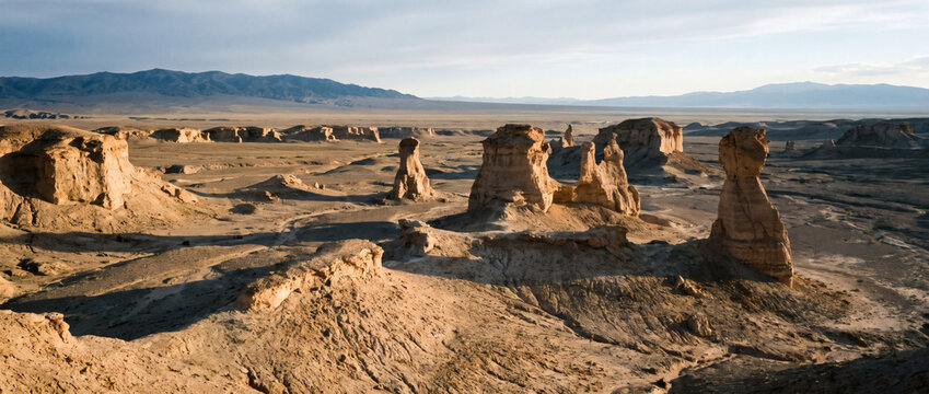 Arid desert landscape with eroded rock formations under soft light, distant mountains on the horizon.