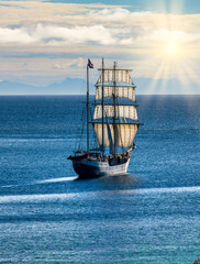 Traditional sailing ship cruises off Nusfjord, with the mountain silhouettes of the Lofoten Islands visible on the horizon. © EKH-Pictures
