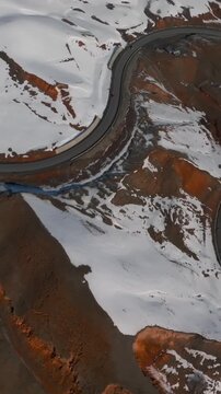 Drone footage looking straight down on a curving asphalt road crossing snowy mountain slopes at Chyyyrchyk Pass, Kyrgyzstan, with exposed brown rock and ridges