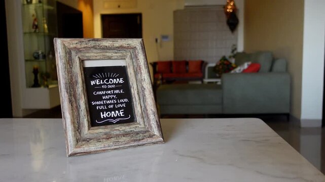 A rustic wooden decorative frame with a welcoming home message placed on a table inside a living room