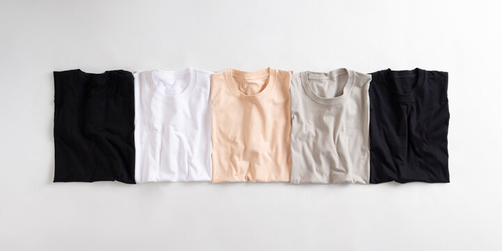 A row of folded casual cotton t-shirts in neutral colors arranged neatly on a white background