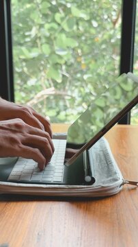 Close-up of hands typing on a portable tablet keyboard, working remotely from a cafe.