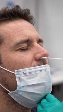 Medical diagnostic test shows man squinting eyes tightly while gloved technician performs nasopharyngeal screening swab in clinic environment before male patient breathes relief upon completion.