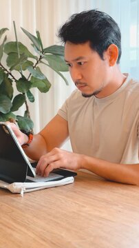 Focused Asian Man Working Remotely on Tablet with Keyboard at Wooden Table