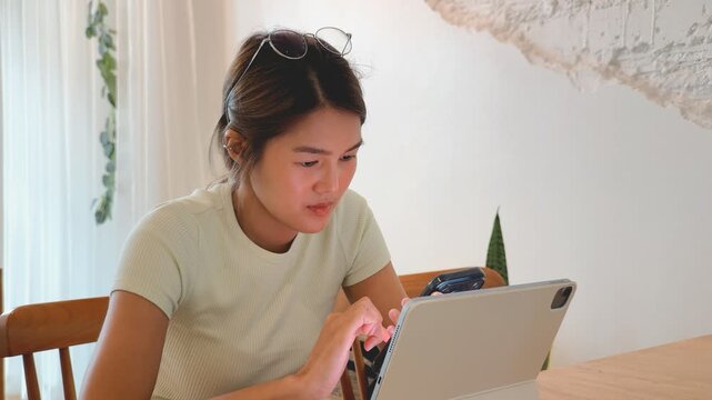 Young Asian Woman Working Remotely with Tablet and Smartphone in a Bright Modern Cafe