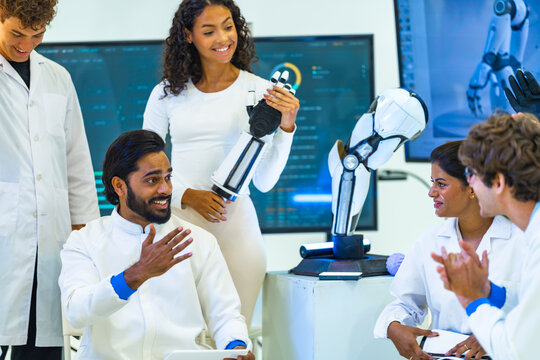 Cheerful robotics team claps and laughs as curly-haired woman shows off a working bionic hand beside a humanoid robot arm, while ideas are exchanged, a smart automation concept