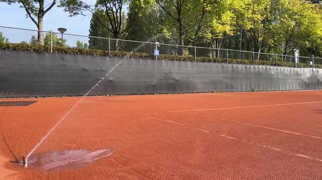 Gravel tennis courts are being watered after play and before the next match to maintain surface quality. 