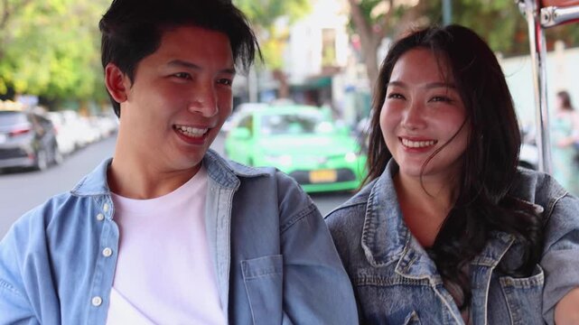 Happy young Asian couple smiling and riding tuk tuk vehicle around city in Thailand, cheerful tourist man and woman enjoying local transportation, travel vacation, tourism, romance and journey concept