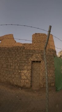 Old stone and mud-brick building ruins behind a barbed-wire fence in Saudi Arabia.
