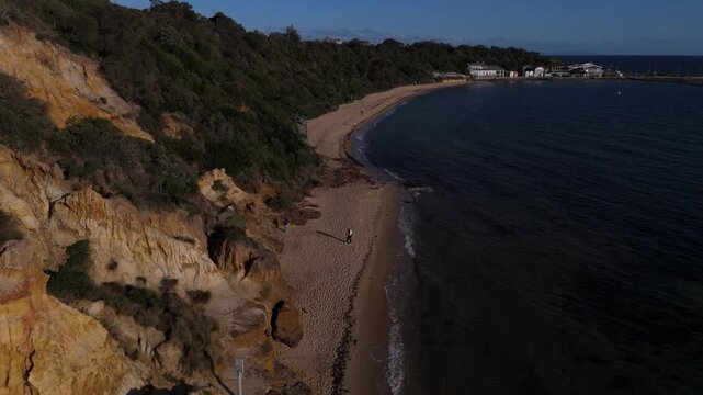 Aerial view flying forward along sandy beach and red sandstone cliffs at Red Bluff