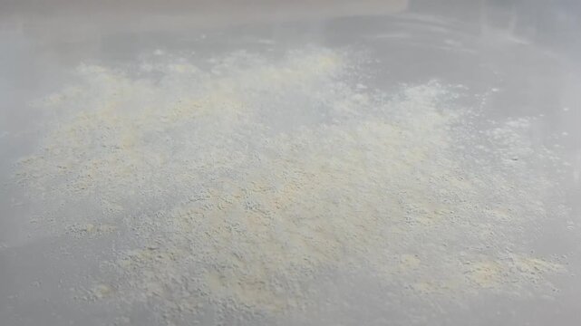 Fine white flour falling and dusting onto a clean kitchen table for baking preparation