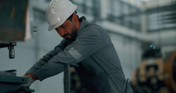 Factory worker in hard hat and gloves operating metal press machine on production floor