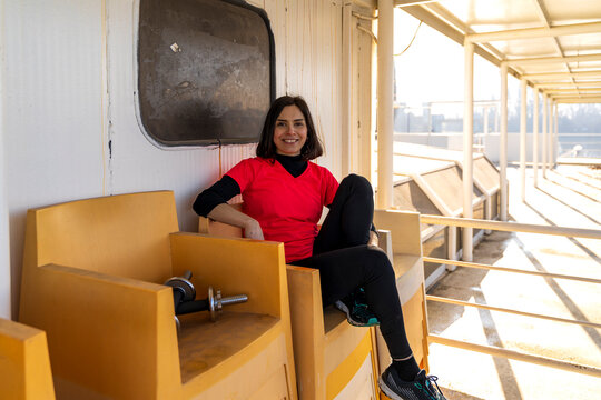 Smiling woman taking a break from exercise, sitting on a bench with a dumbbell