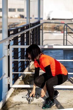 Woman squatting down, picking up dumbbells for a workout on a sunny day