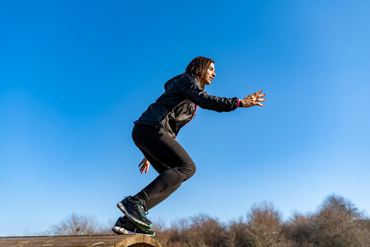 Woman jumping over a wooden log during outdoor exercise against a clear blue sky