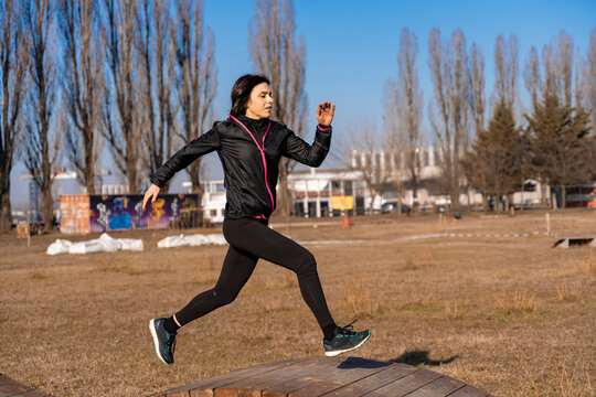Young woman actively training, jumping over a wooden obstacle outdoors in urban parkour
