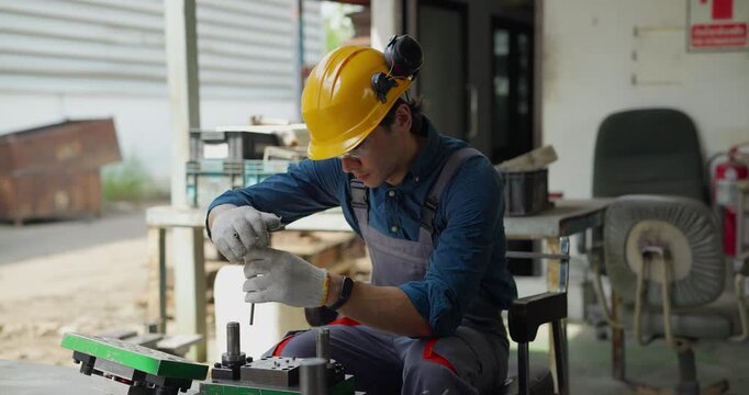 Factory worker in hard hat using tools to file metal part in bench vise at workshop