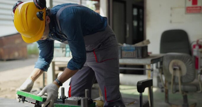 Factory worker in hard hat using tools to file metal part in bench vise at workshop
