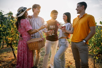 Obraz premium Group of young friends toasting with glasses of red wine in vineyard