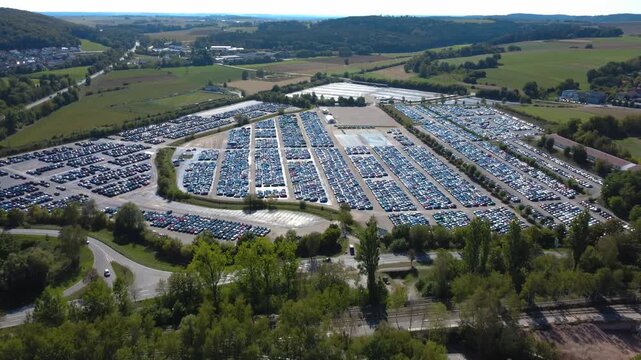 Drone aerial approaching a huge car terminal with thousands of new vehicles parked in dense organized rows. Large vehicle storage and distribution facility in Kelheim, Bavaria, Germany