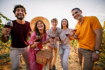 Obraz premium Group of smiling friends posing closely with red wine in sunset vineyard