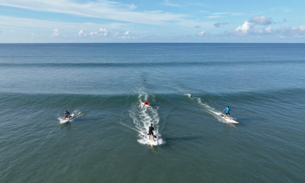 aerial drone shot taken high ocean surface capturing three surfers paddling towards waves distance bright sunny
