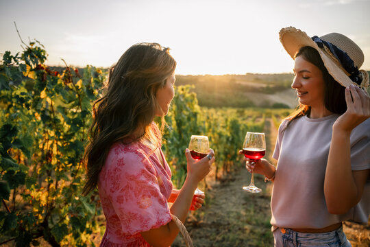 Two young women enjoying wine and talking in a lush vineyard row